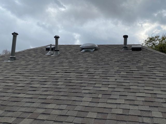 Gray shingle roof with several vents and a skylight under a cloudy sky.