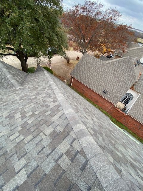 View from a roof with gray shingles, trees, and a brick building in the background.