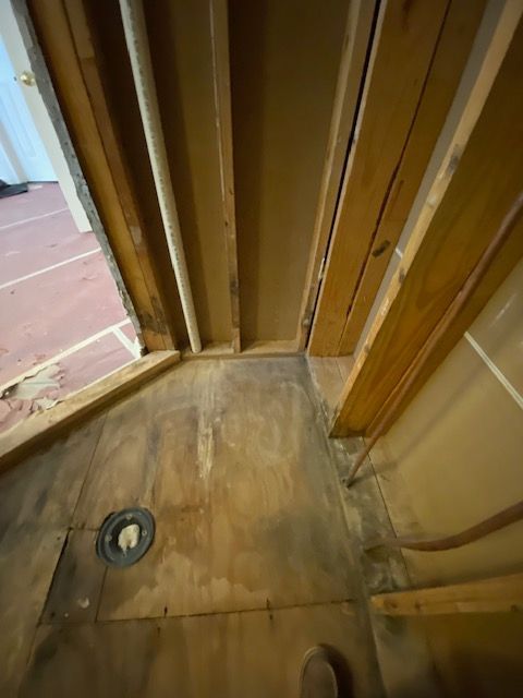 Interior view of a shower construction with exposed wood framing, plumbing, and a drain.