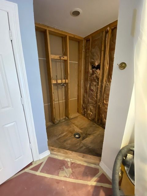Bathroom under construction with exposed framing, insulation, and a drain.