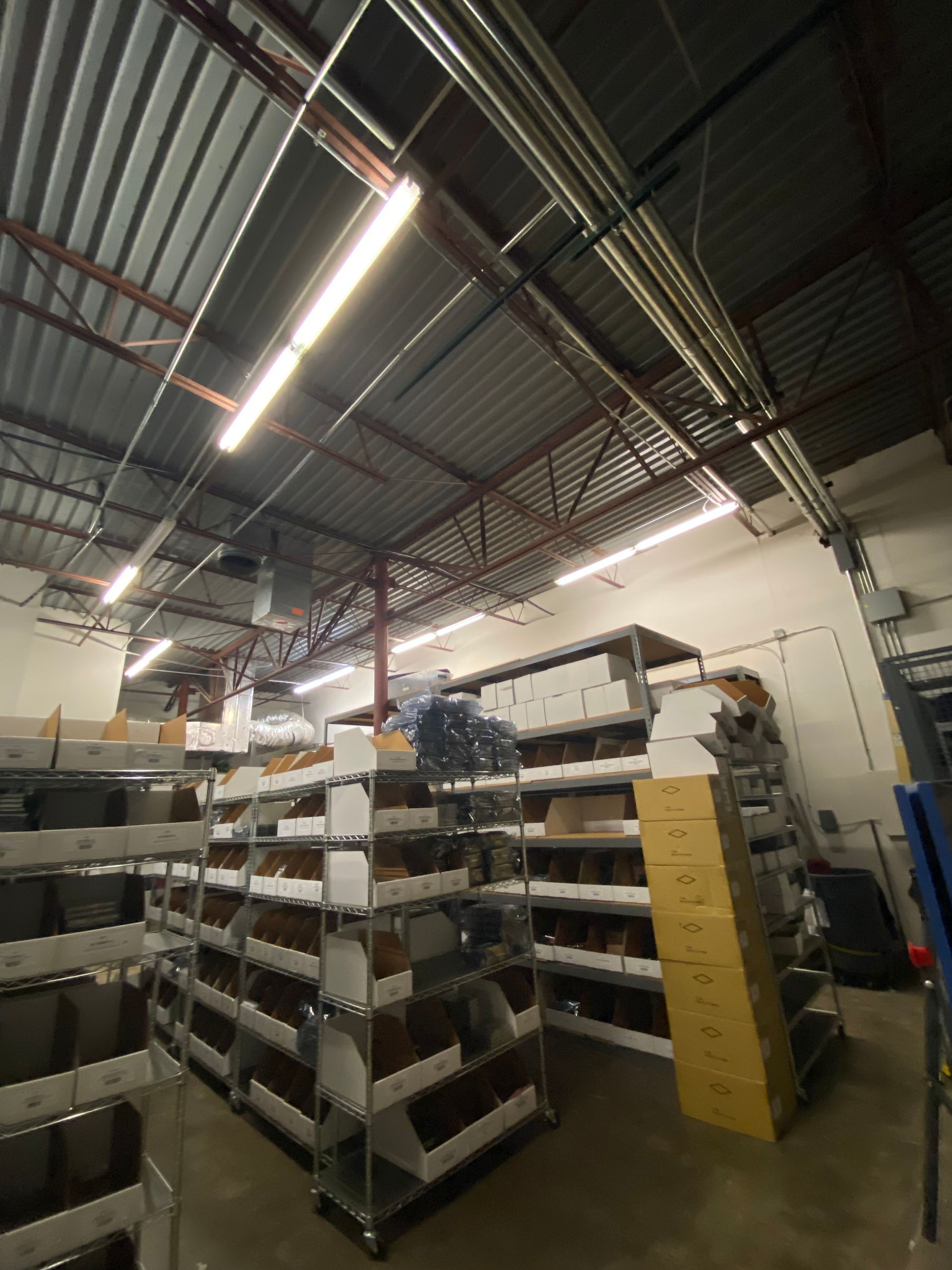 Warehouse interior with metal shelving filled with bins and boxes, lit by fluorescent lights.