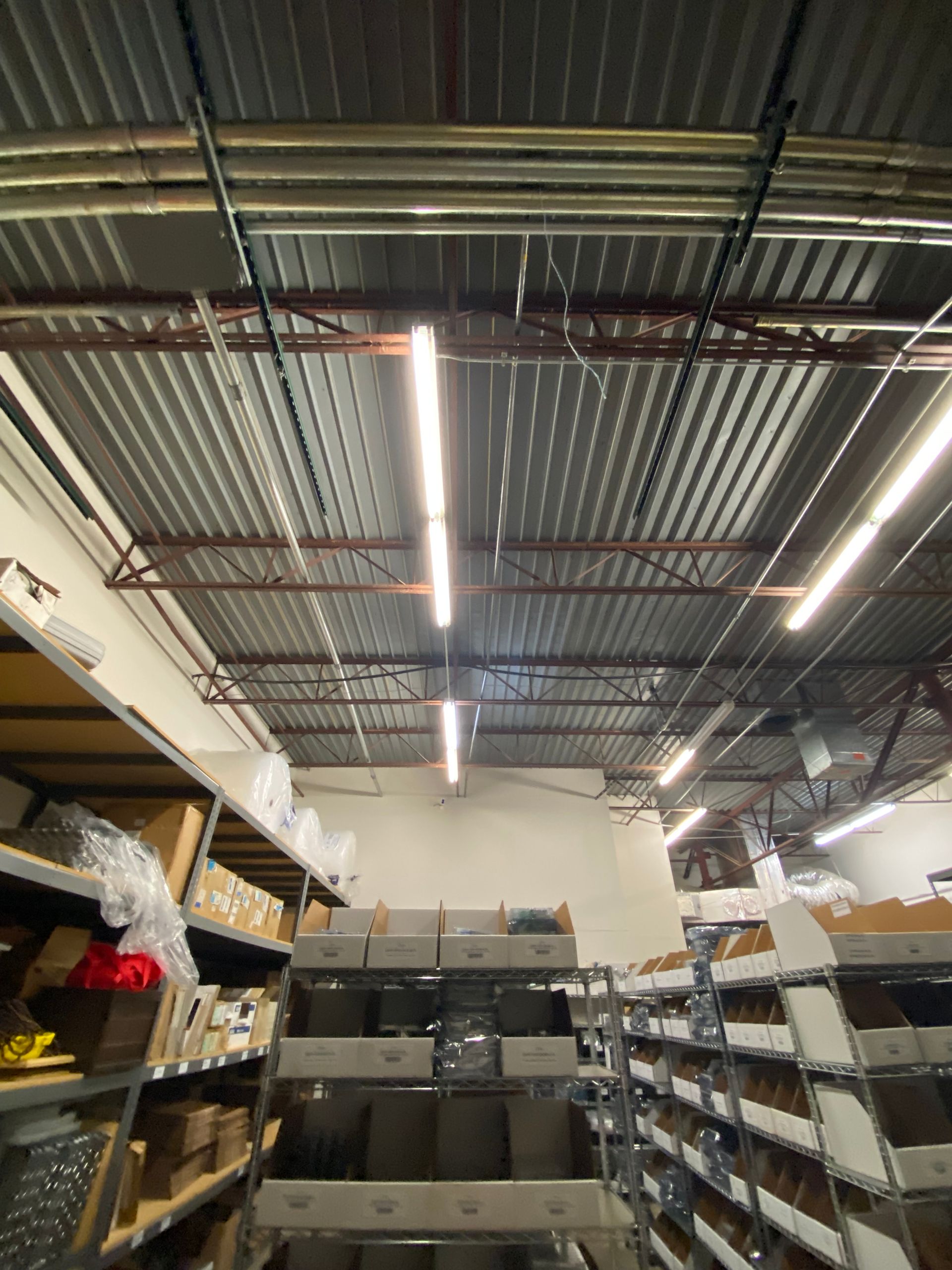 Warehouse interior with shelves of boxes and fluorescent lighting in the ceiling.