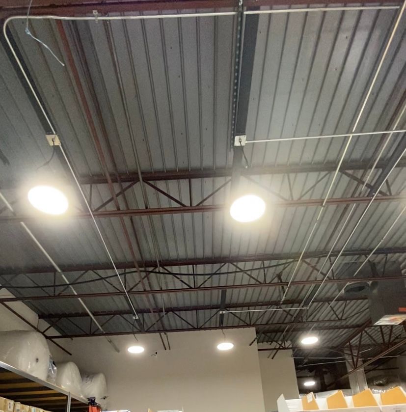 Warehouse ceiling with metal beams, bright lights, and electrical conduit.