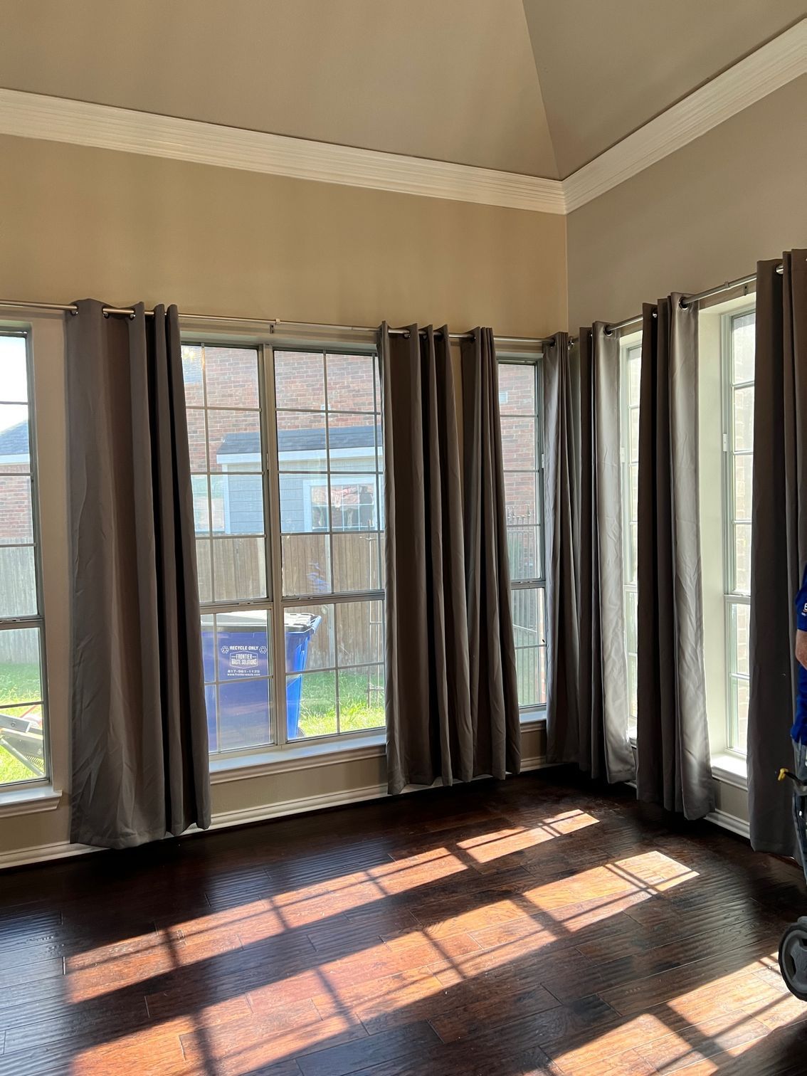 Gray curtains frame multiple windows in a room with a dark wooden floor.