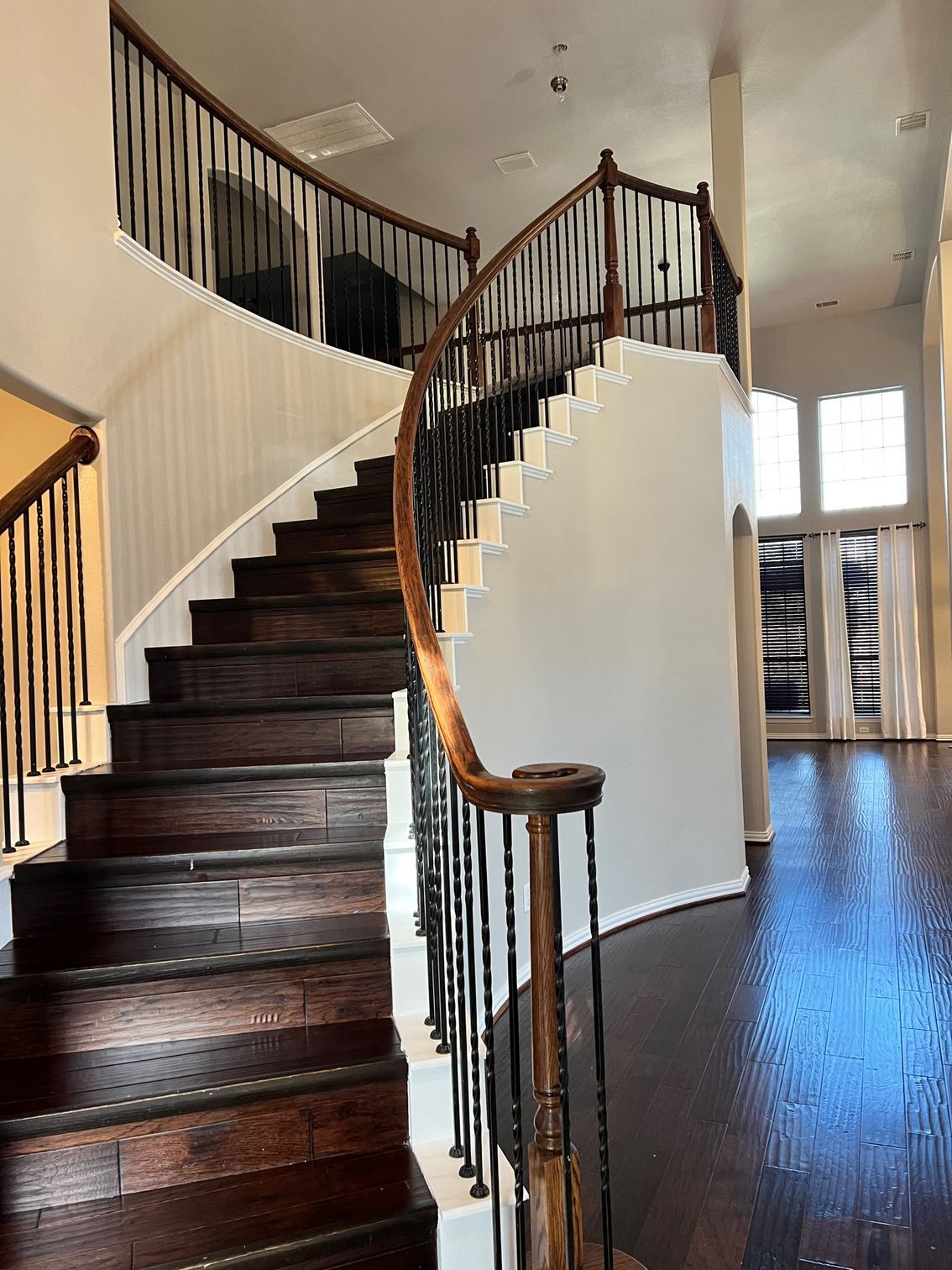 Dark wooden spiral staircase with wrought iron railing in a home.