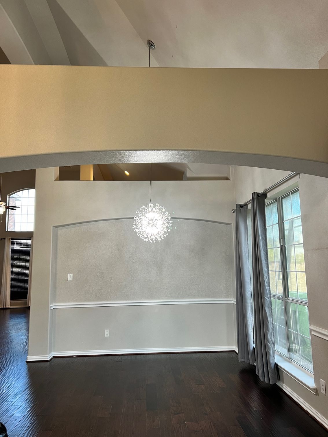 Dining room interior with a chandelier, window, and dark wood floor.