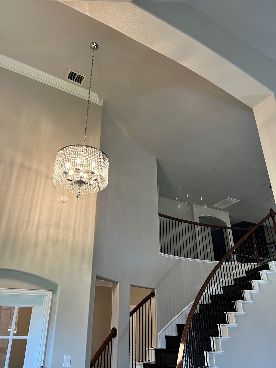 A crystal chandelier hangs in a high-ceilinged entry. Staircase with black and white steps leads upwards.
