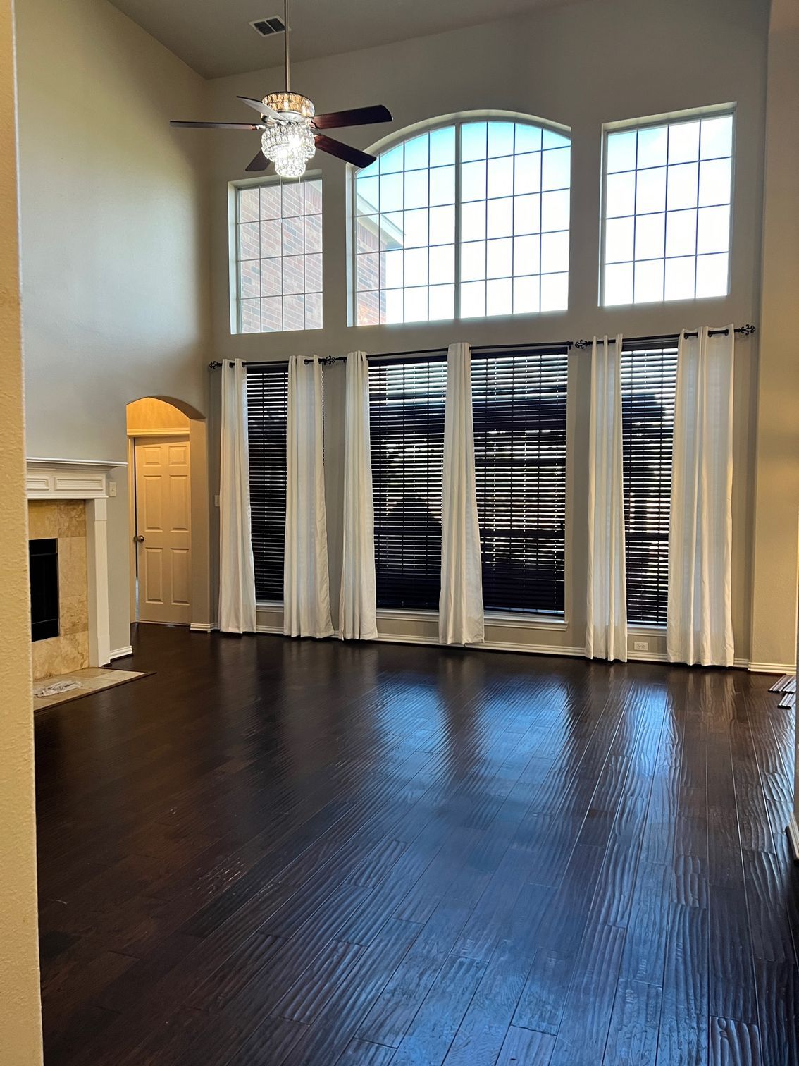 High-ceilinged living room with tall windows, dark wood floors, and white curtains.