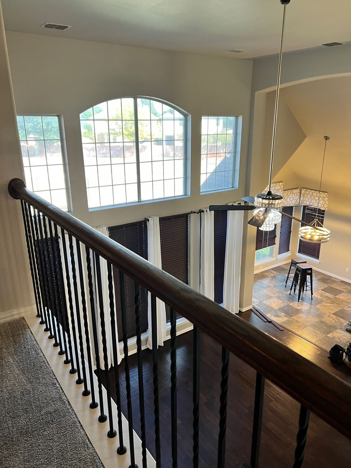 View from a staircase railing, looking down into a well-lit living room with tall windows and curtains.