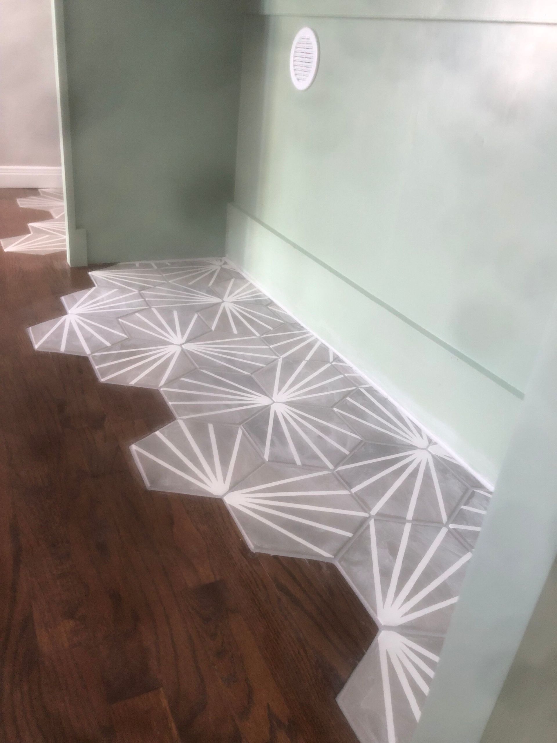 Hexagon tile floor with gray and white pattern meeting dark wood flooring.