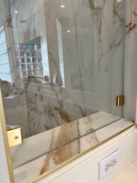 Shower with marble walls, glass door, and gold hardware.