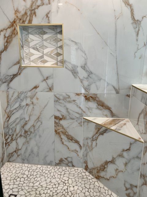 Marble shower with pebble floor, geometric tile niche, and triangular bench.