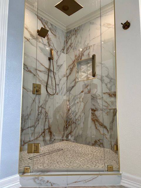 Marble-tiled shower with glass doors, brass fixtures, and pebble flooring; modern bathroom.