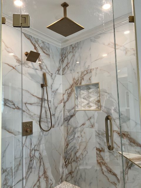 Marble-tiled shower with glass doors, bronze fixtures, and a built-in shelf.