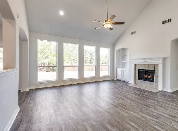 Spacious living room with large windows, fireplace, vaulted ceiling, and gray wood flooring.
