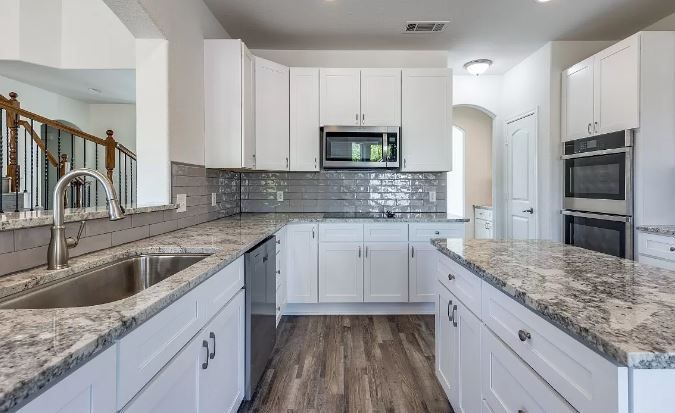 White kitchen with granite countertops, stainless steel appliances, and a gray backsplash.