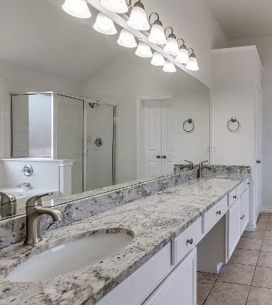 Bathroom with a long countertop, two sinks, a large mirror, and bright overhead lighting.