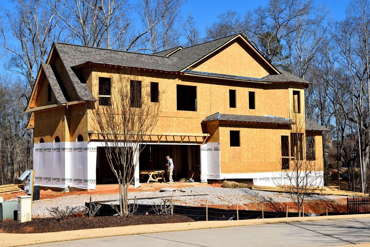 Two-story house under construction with exposed wooden frame and a worker inside the garage.