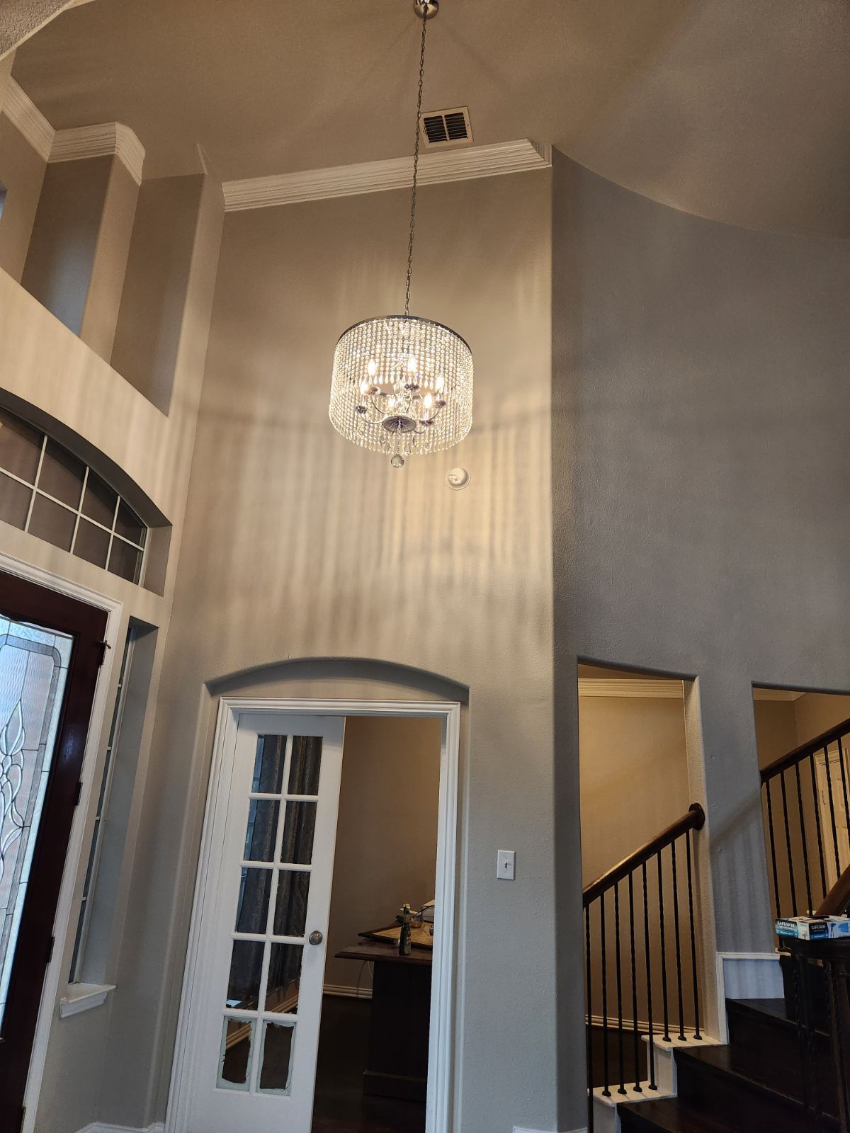 A tall foyer with a crystal chandelier, doors, and a staircase.