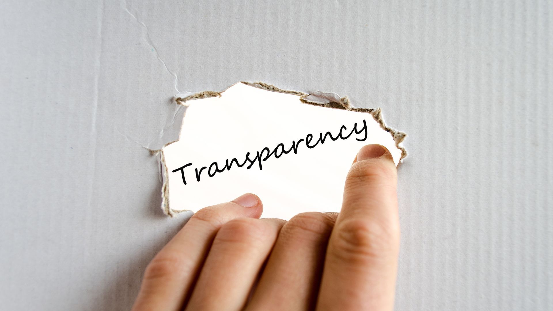 A hand tears away a piece of a plain white wall to reveal the handwritten word 