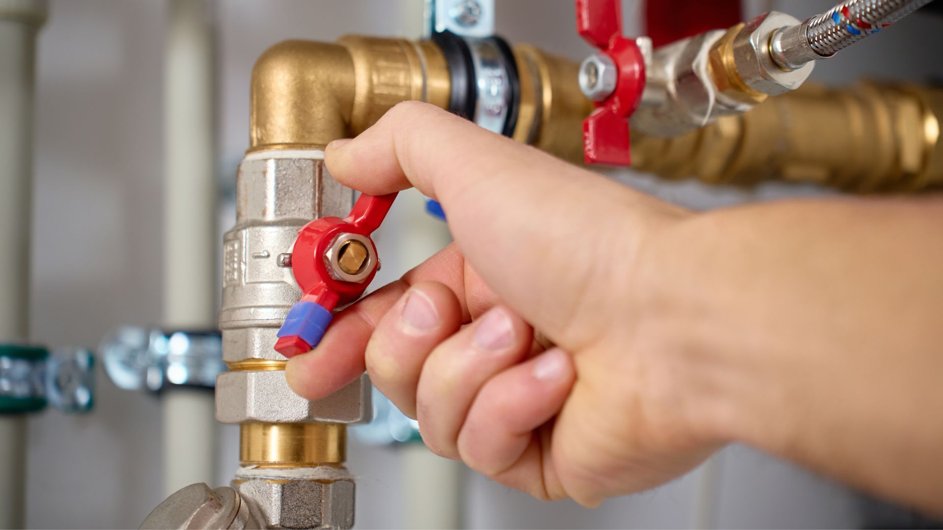 A hand turns a red ball valve on a brass plumbing pipe assembly.