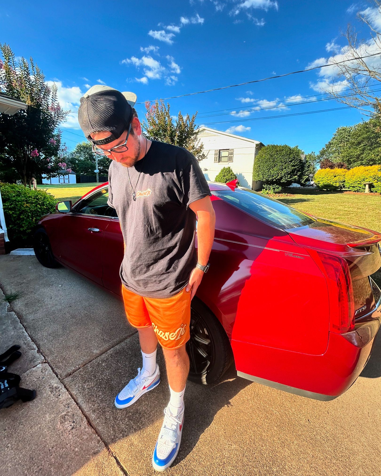 A man is standing next to a red car in a driveway.