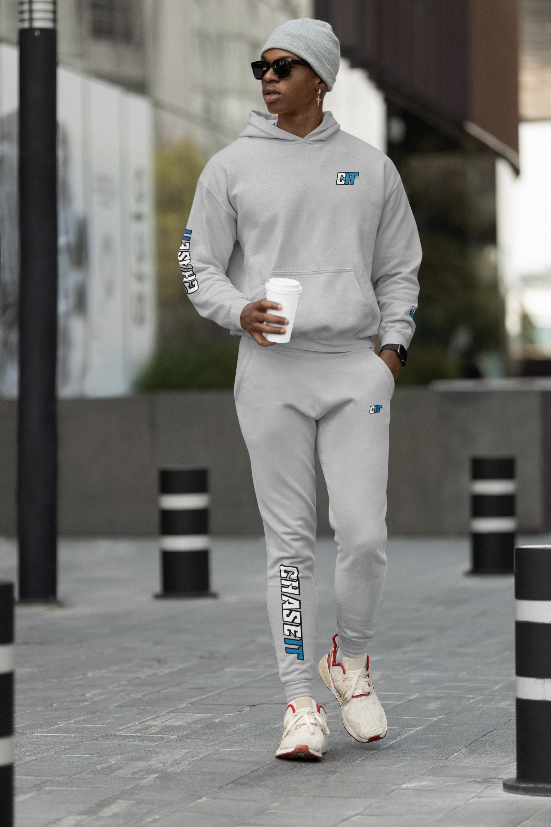 A man wearing a hoodie and sweatpants is walking down the street holding a cup of coffee.