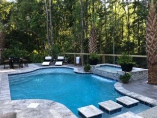 A large swimming pool surrounded by trees and chairs in a backyard.