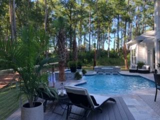 There is a large swimming pool in the backyard of a house surrounded by trees.