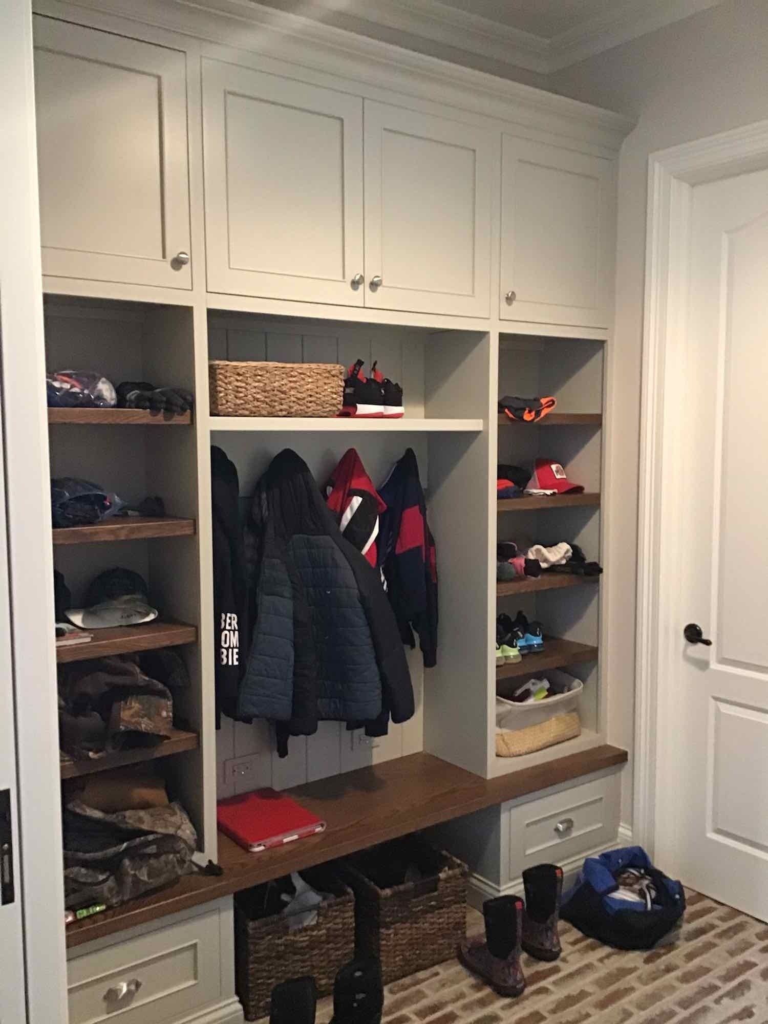 A mud room with a bench and shelves filled with clothes and shoes.