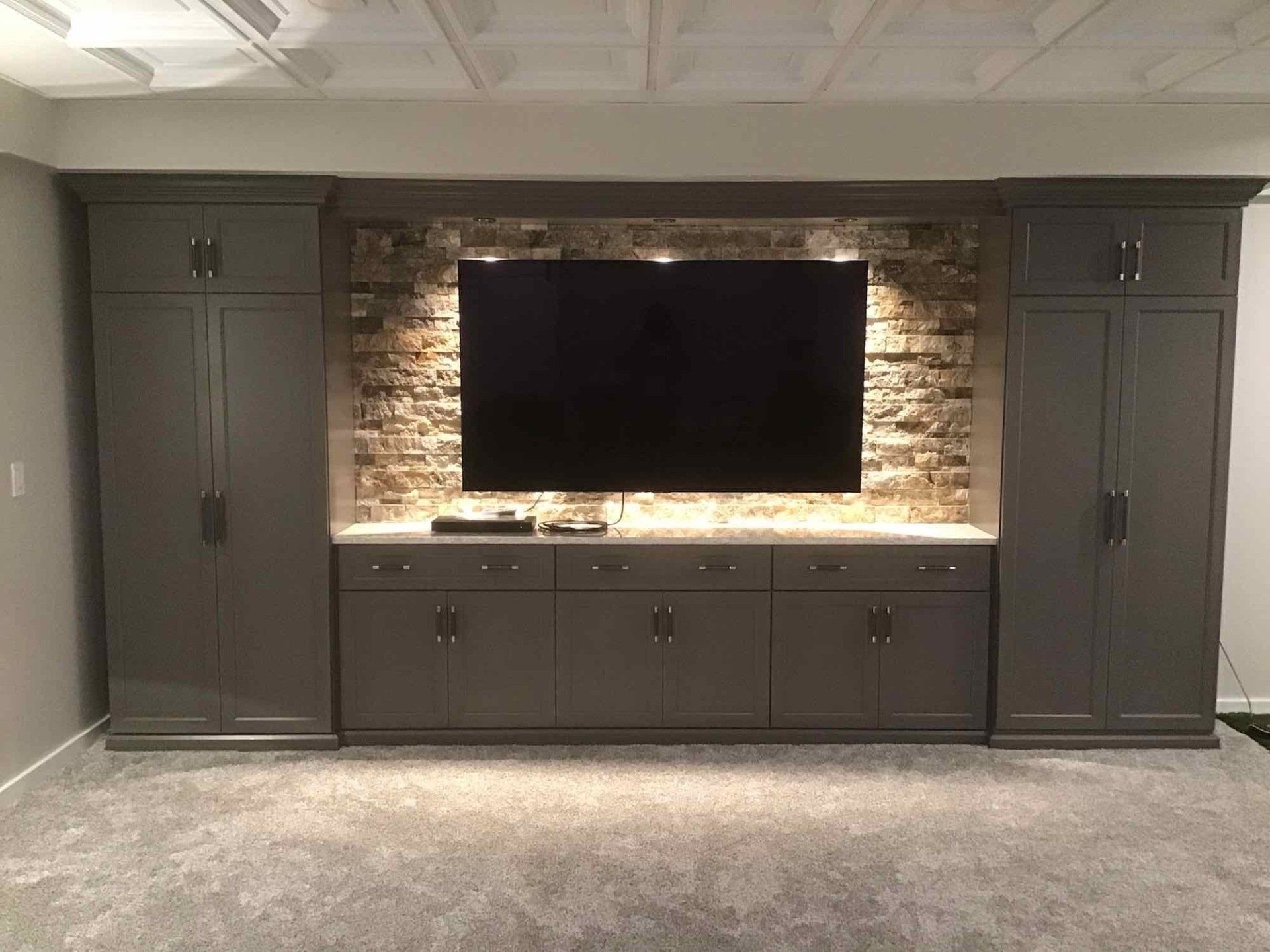 A large flat screen tv is mounted on a wall with custom cabinets in a basement.