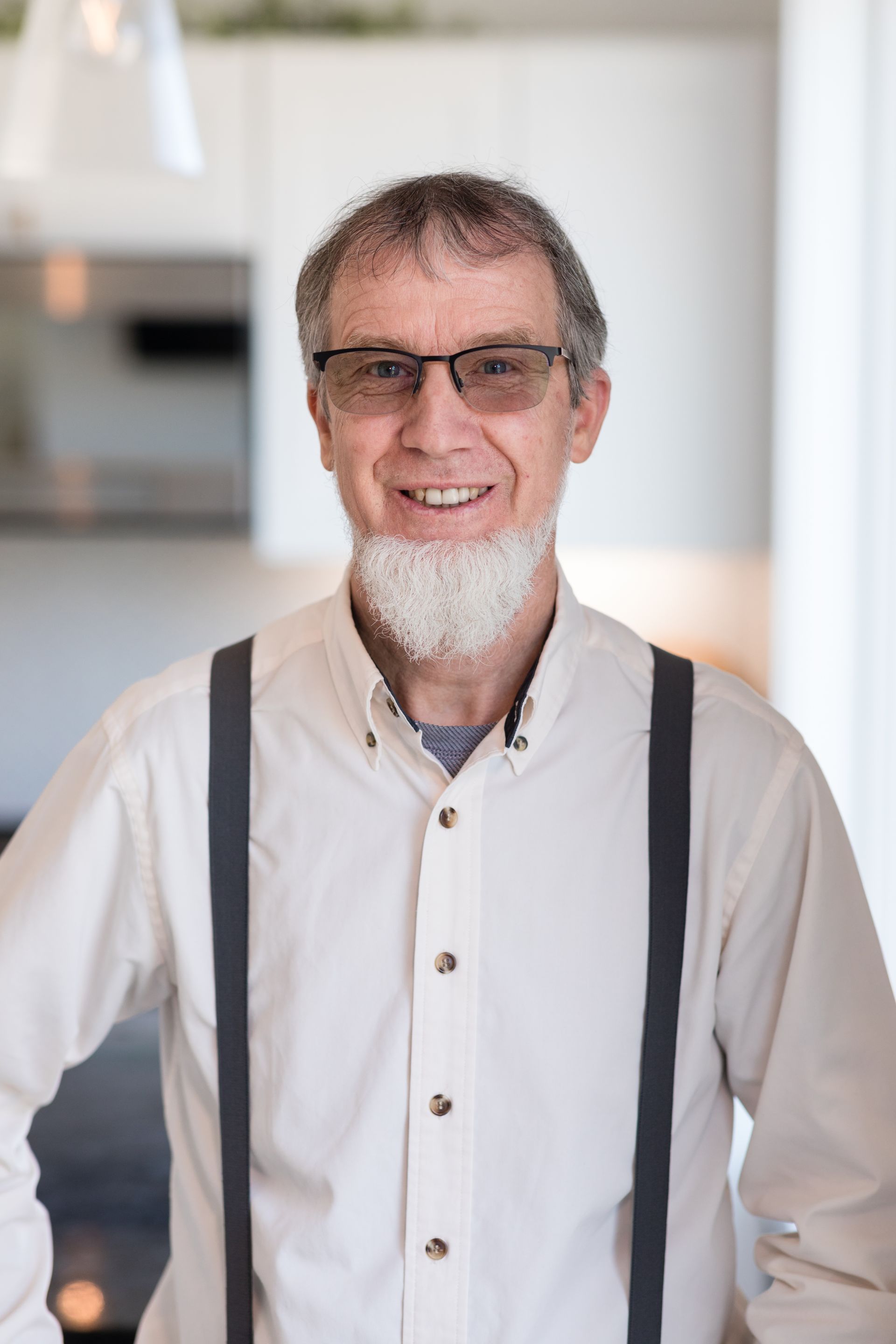 A man with a beard and suspenders is smiling.