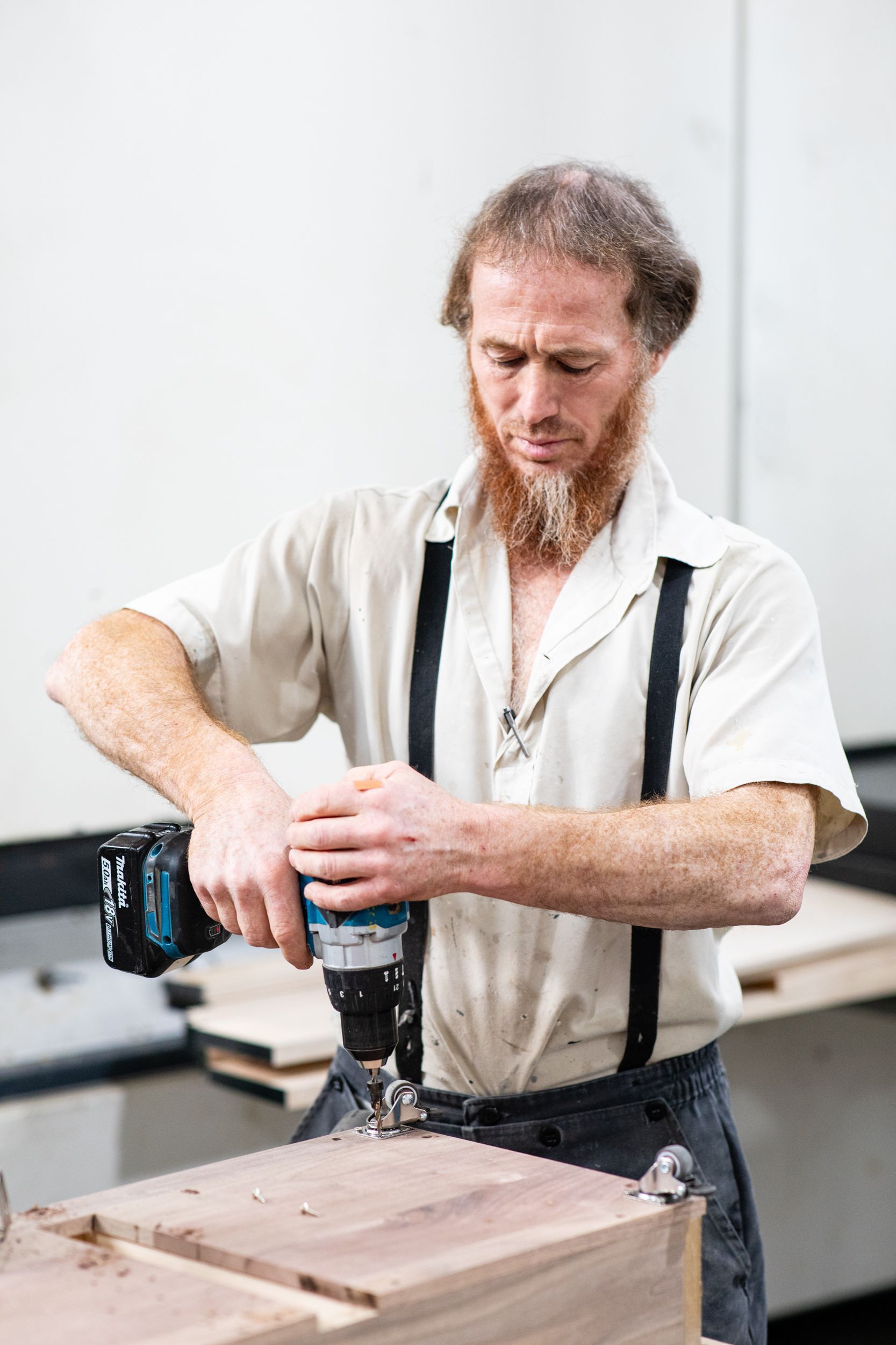 A man with a beard is using a drill on a piece of wood.