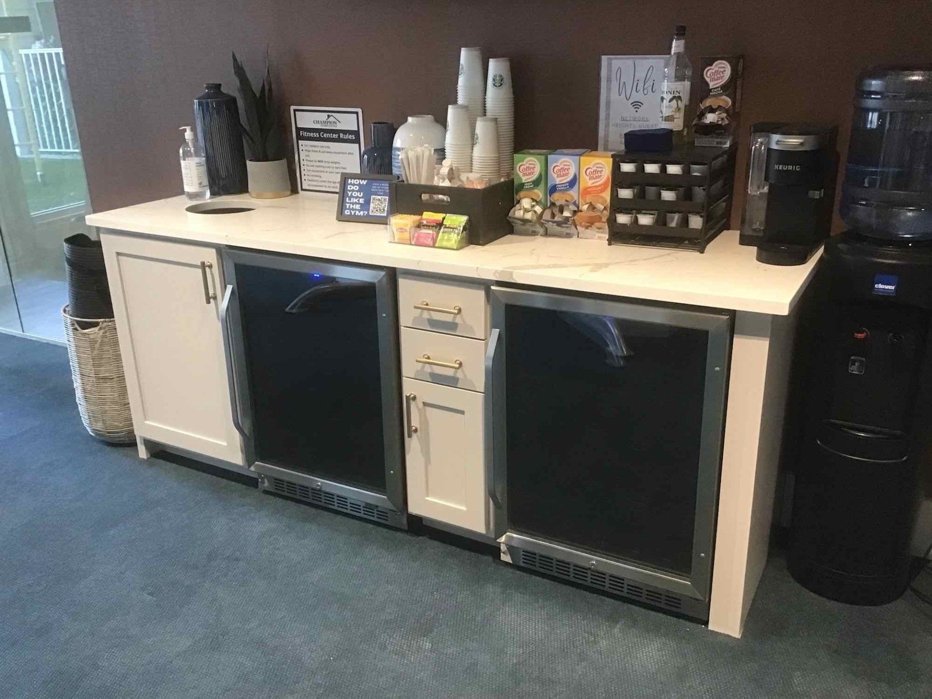 A kitchen counter with a refrigerator, cups, bottles, and other items on it.