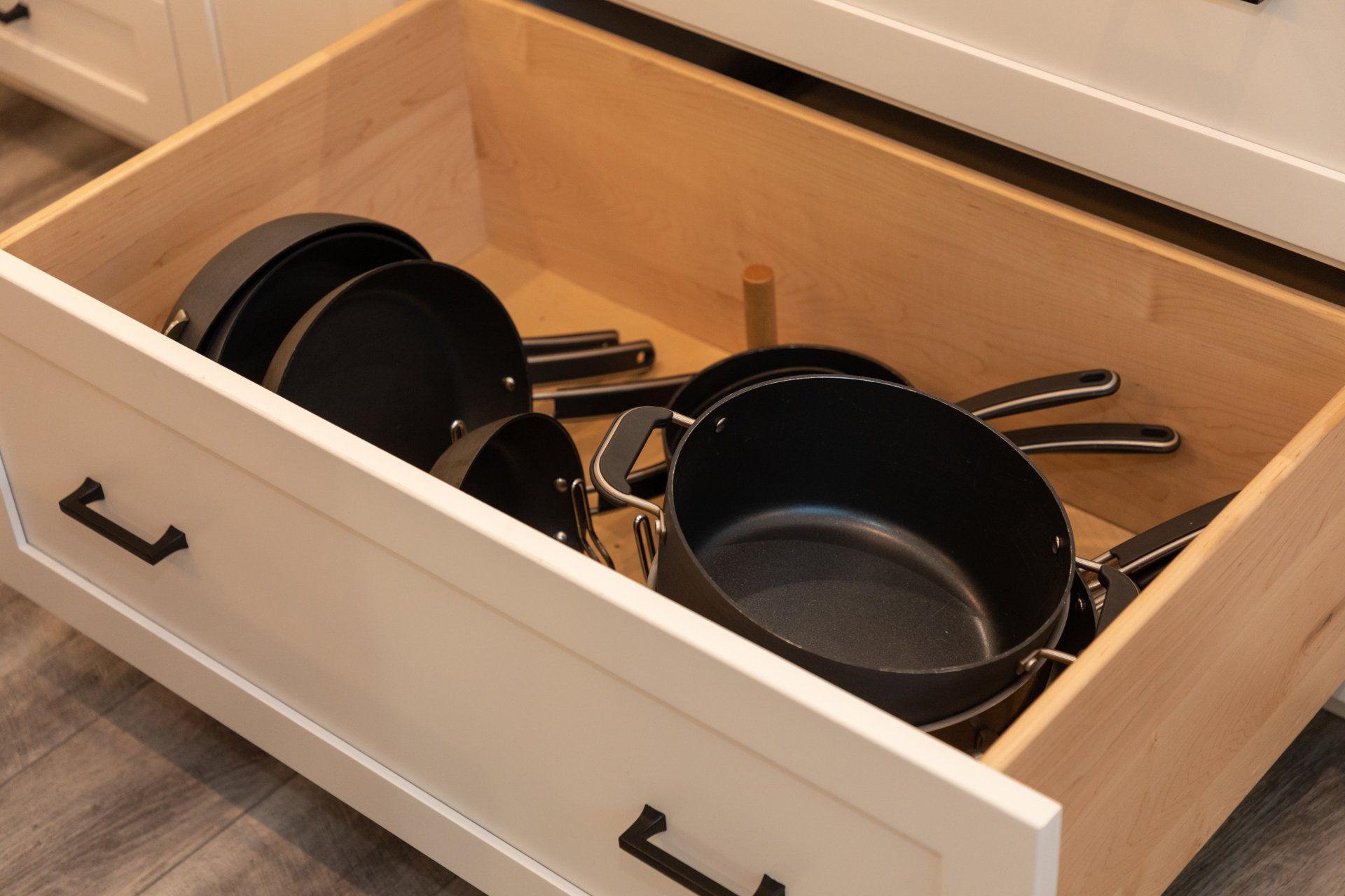 A wooden drawer filled with pots and pans in a kitchen.