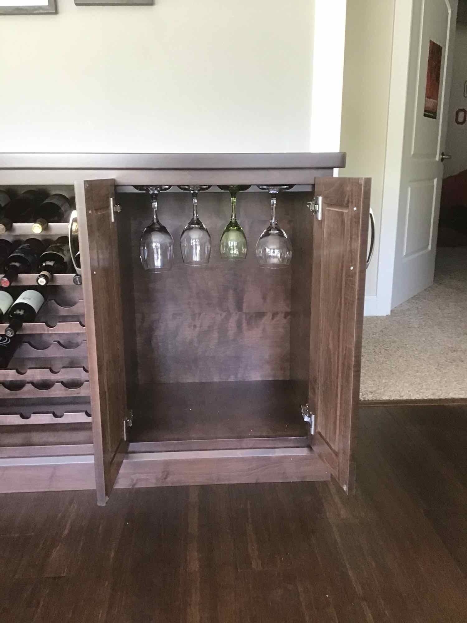A wine cabinet with wine bottles and wine glasses hanging from it.