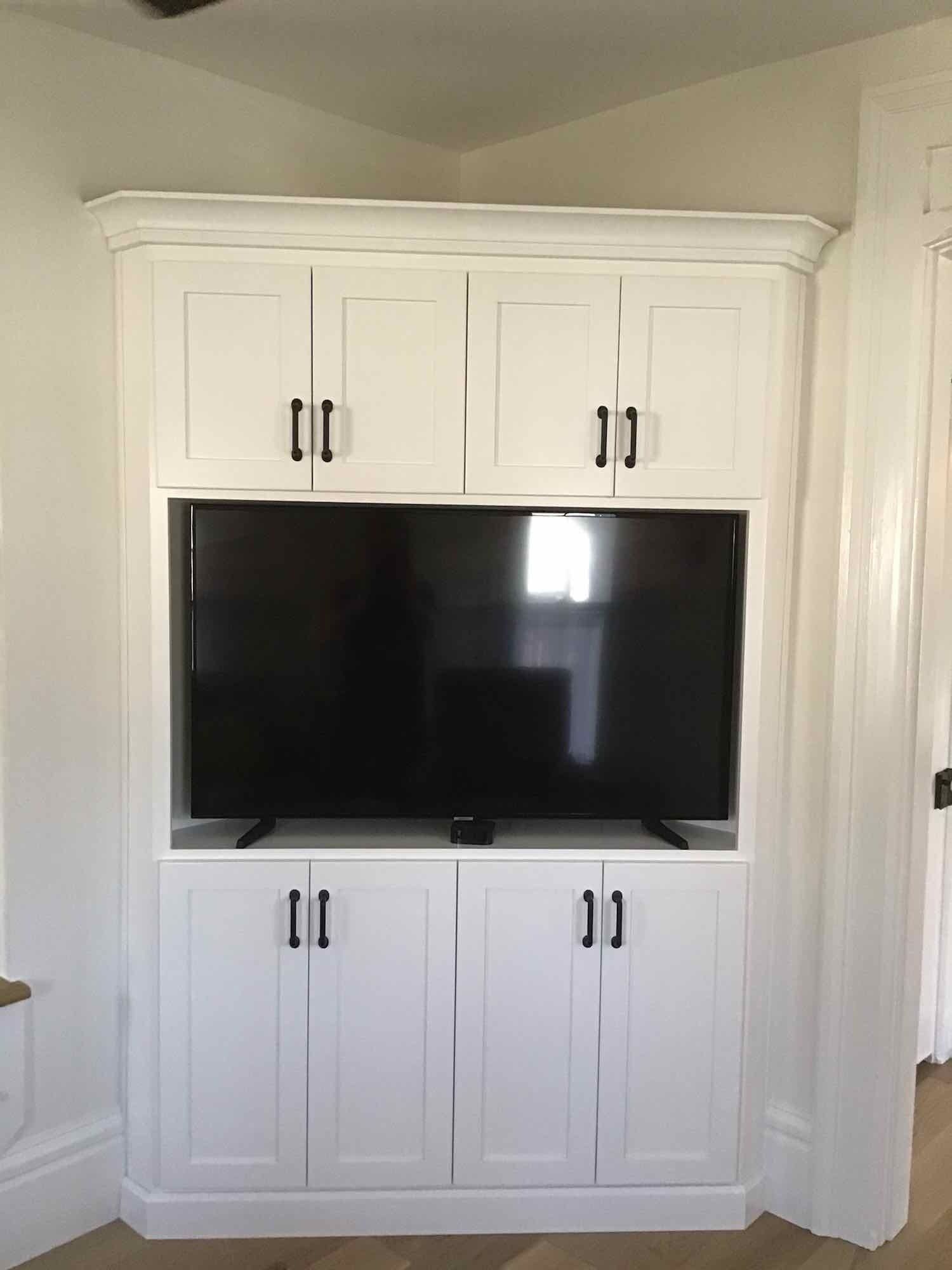 A flat screen tv is sitting on top of white custom cabinets.