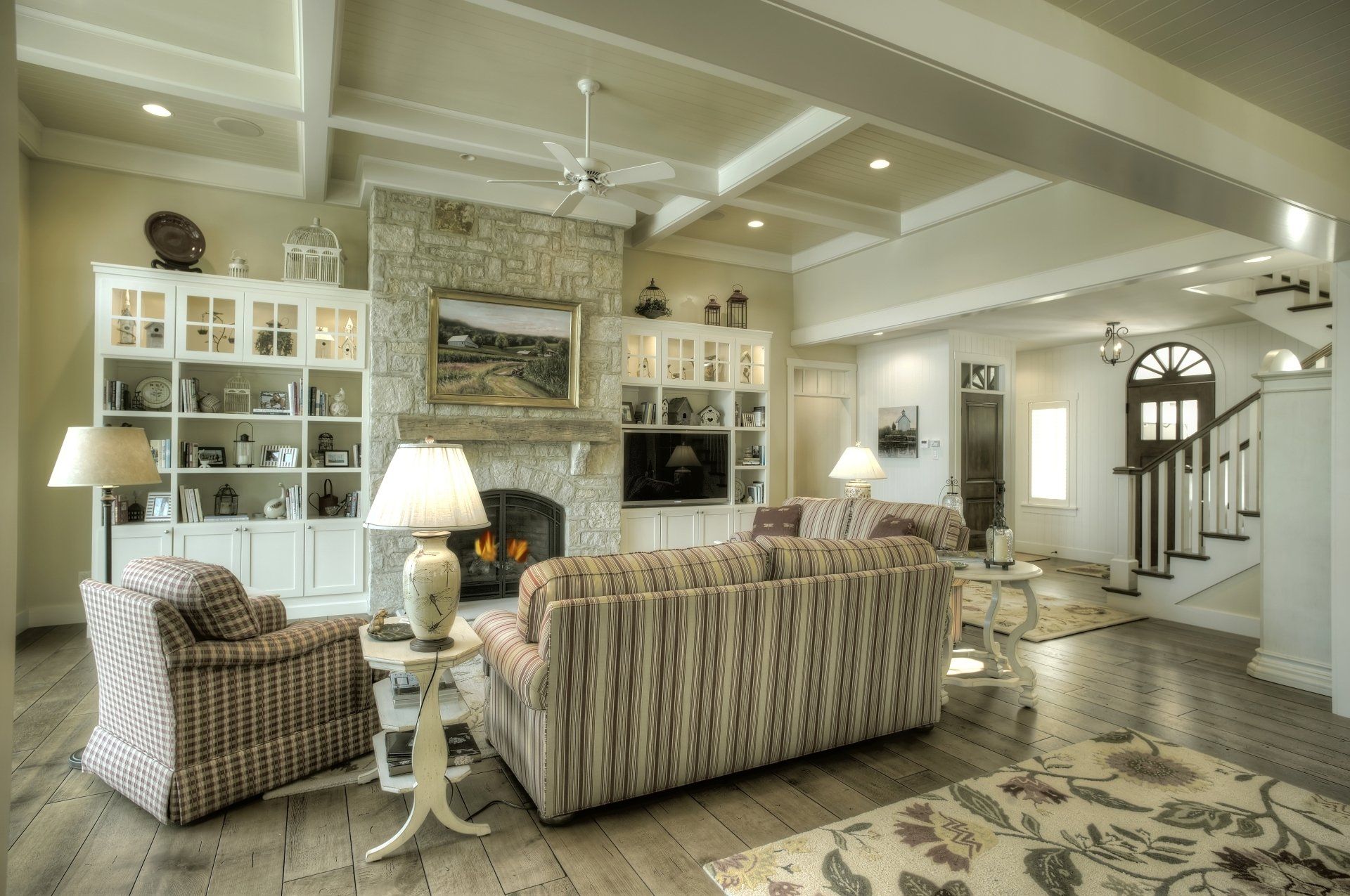 A beautiful living room with built-in cabinets, a couch, chairs, lamps, and a fireplace.