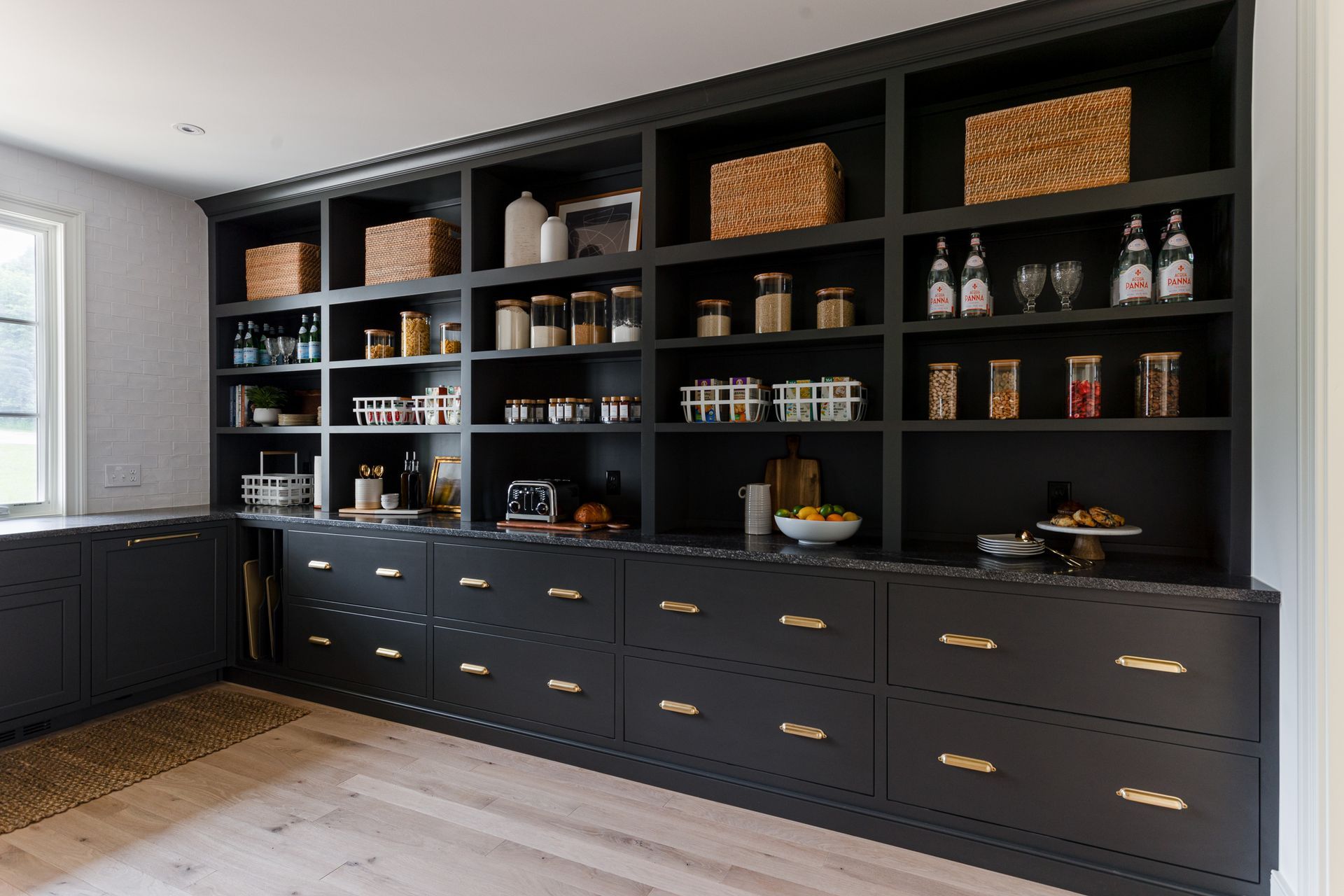 A kitchen with black cabinets, drawers, shelving, and a window.