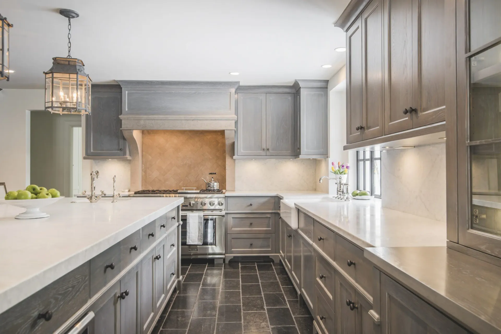 A kitchen with an island, gray custom cabinets, and white counter tops.