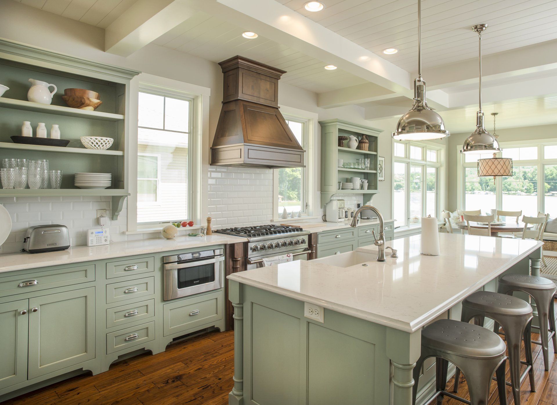 A kitchen with green cabinets, stainless steel appliances, and white counter tops with island. 