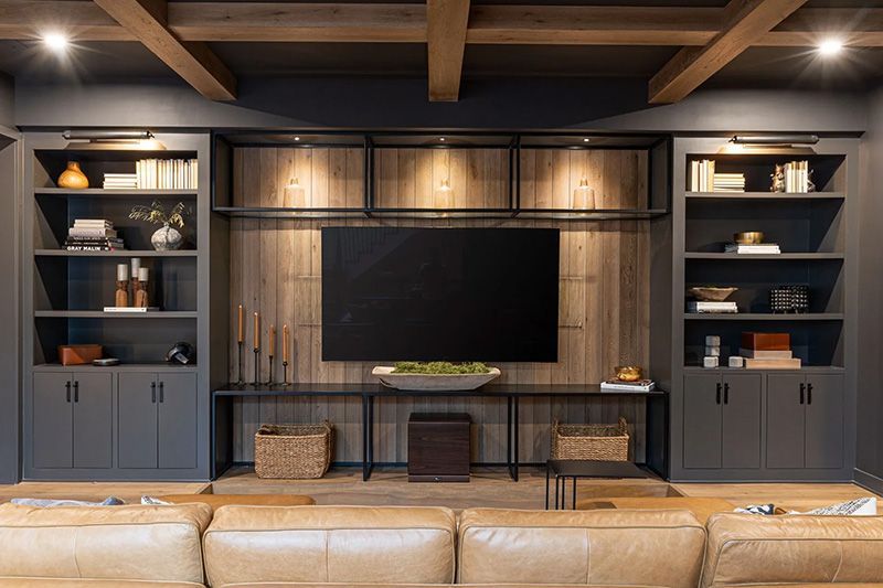 An entertainment room with a couch, shelving, and a mounted flat screen television.