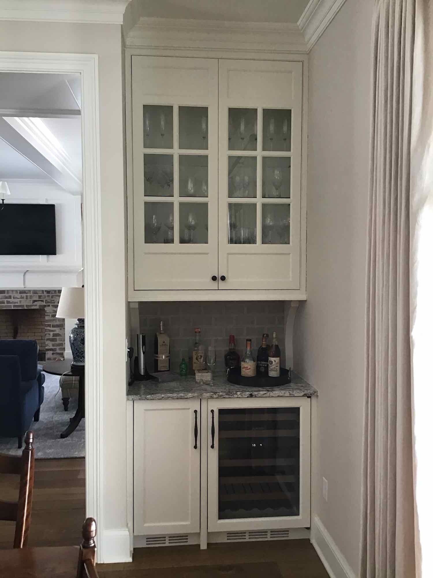 There is a wine cooler in the corner of the room and living room with furnace and fireplace in the background.