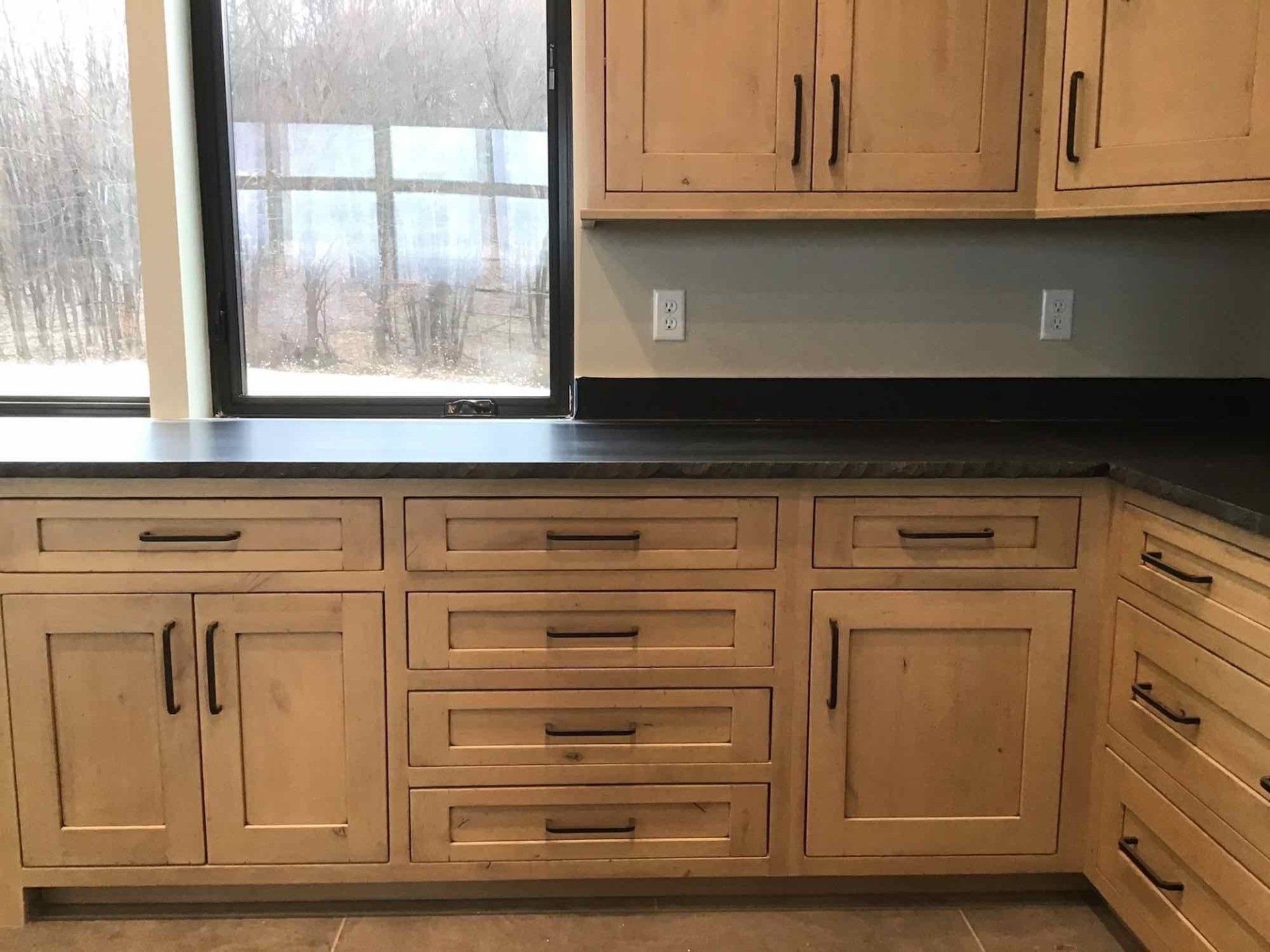 A kitchen with wooden cabinets and drawers and a window