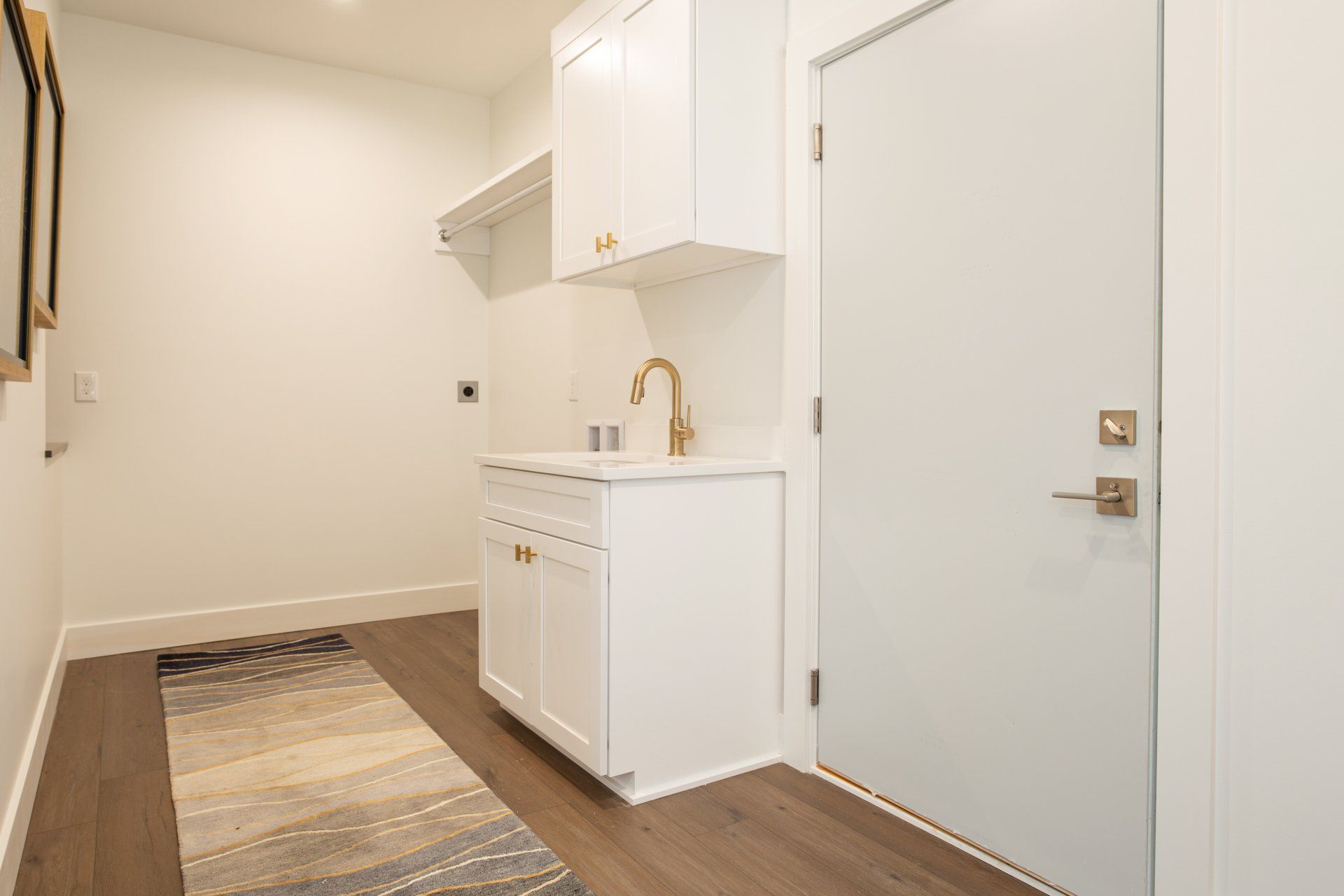A laundry room with a sink, cabinets, and a rug.