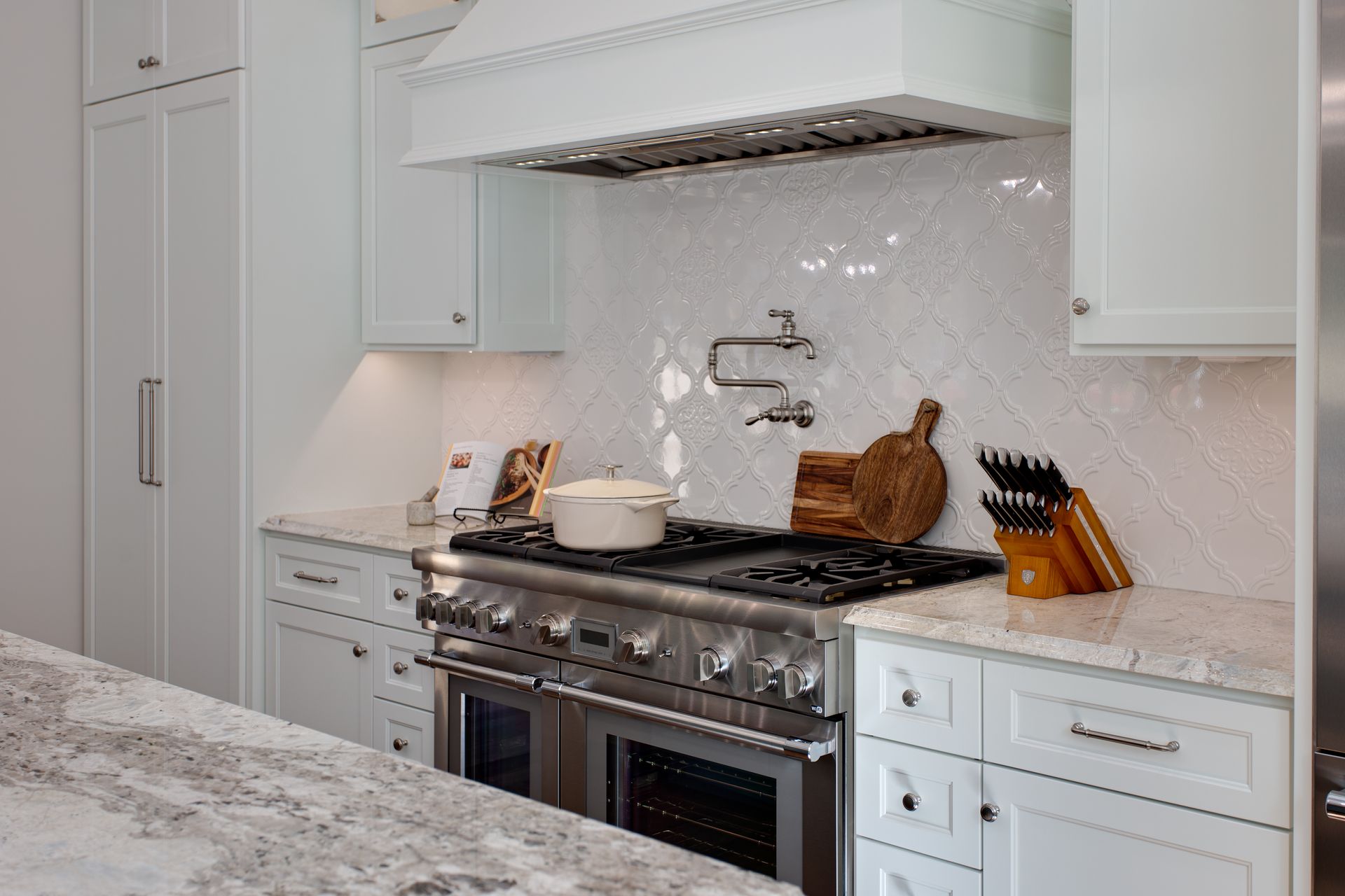 A beautiful kitchen with white cabinets, stainless steel appliances, granite counter tops, and a stove top oven.