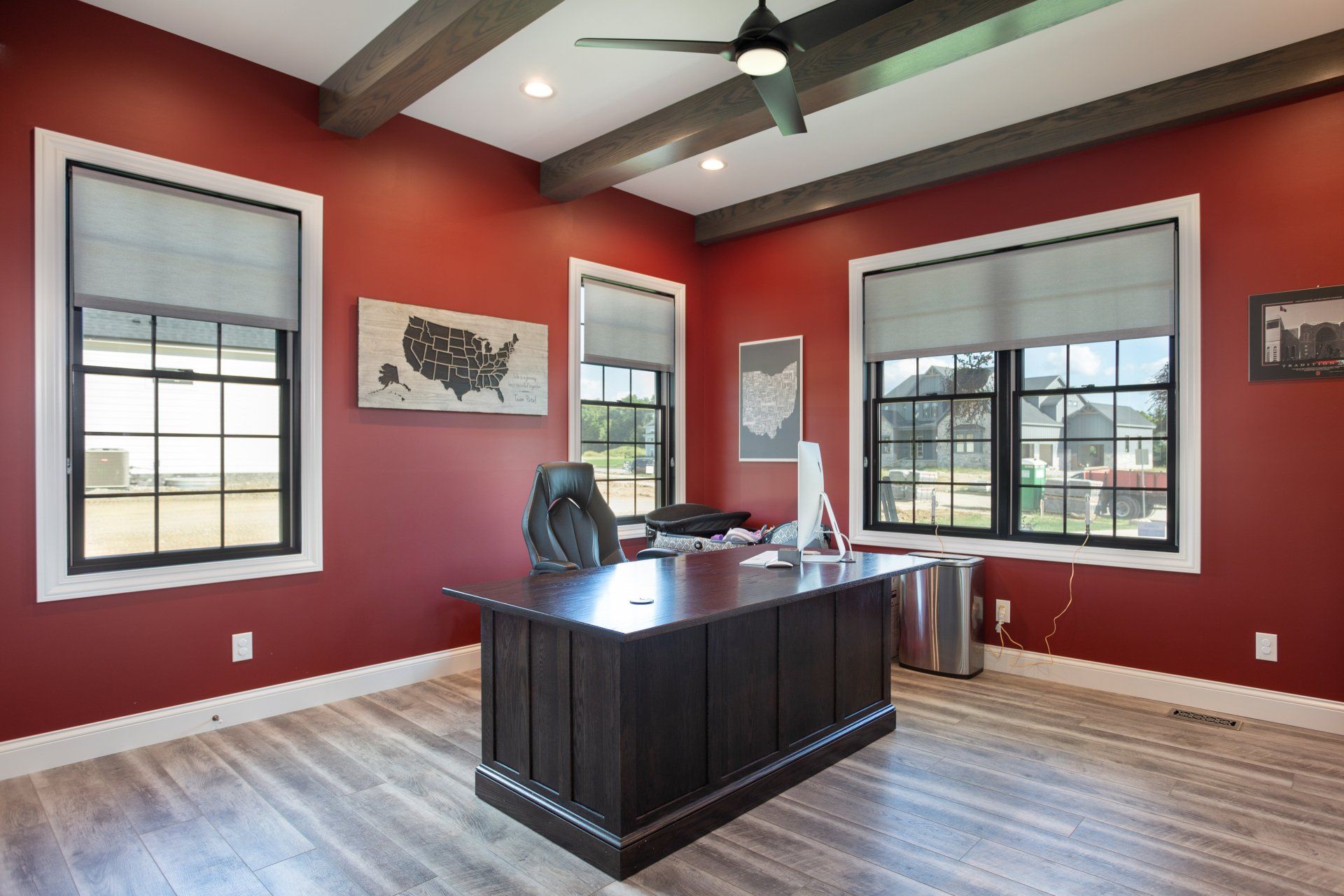 A home office with red walls , a desk and a ceiling fan.