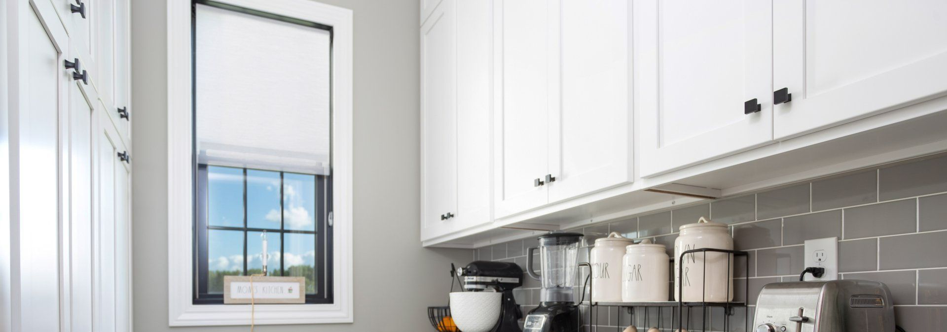 A kitchen with white custom cabinets, a blender, and a window.