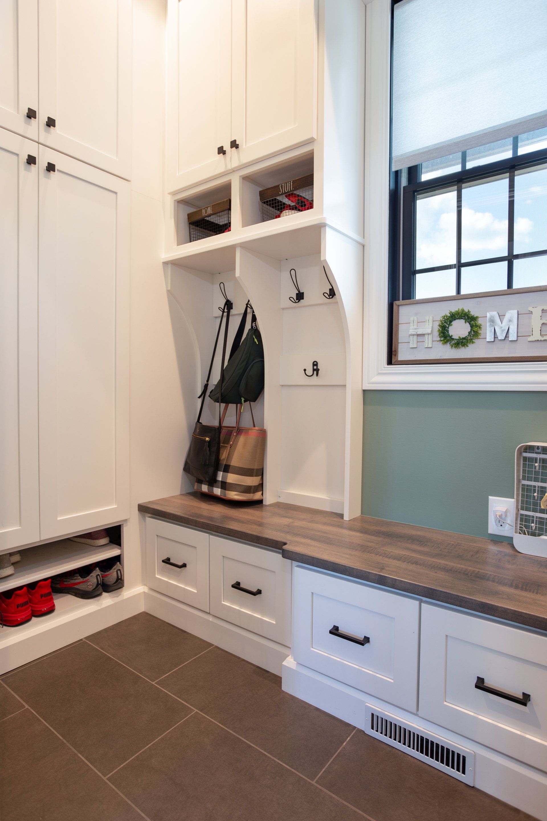 A mud room with white cabinets , drawers , a bench and a window.