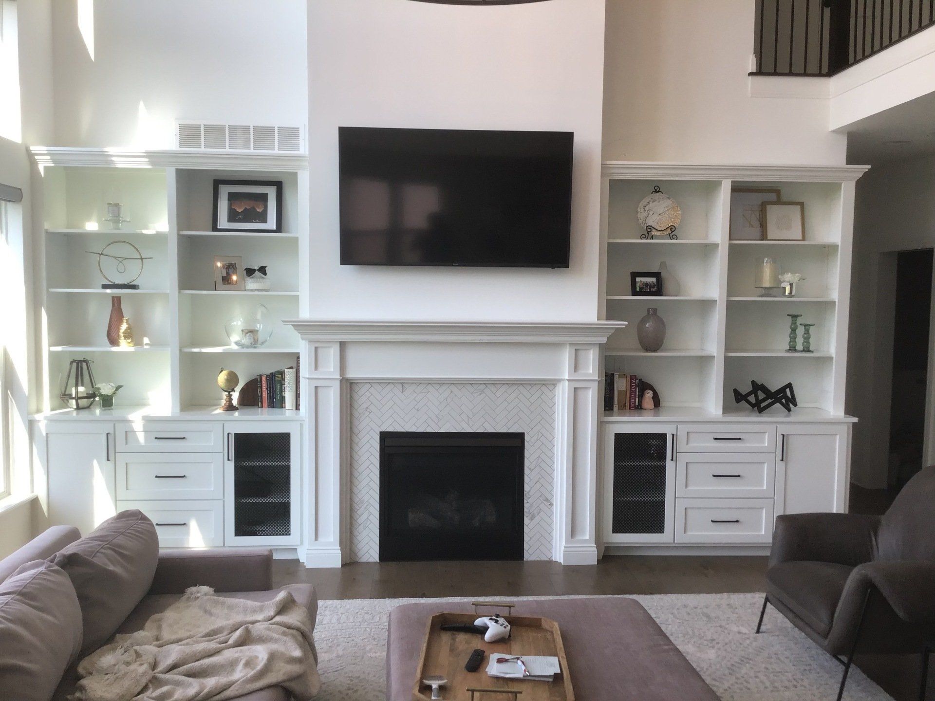 A living room with custom shelf, a fireplace, and a flat screen tv on the wall.